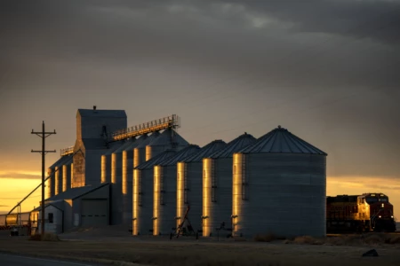 As the sun sets a grain tower becomes a statue of metal covered in golden light. All over the USA countryside grain towers are landmarks connected by railroad. Grain towers with train in golden sun light
